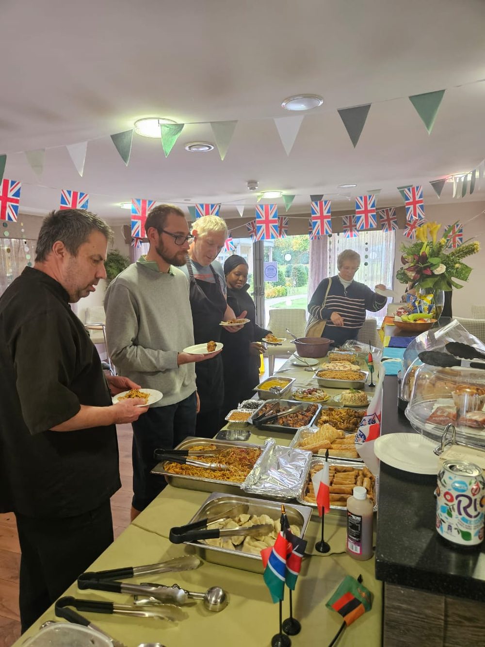 A long buffet table of West African and British dishes with guests helping themselves