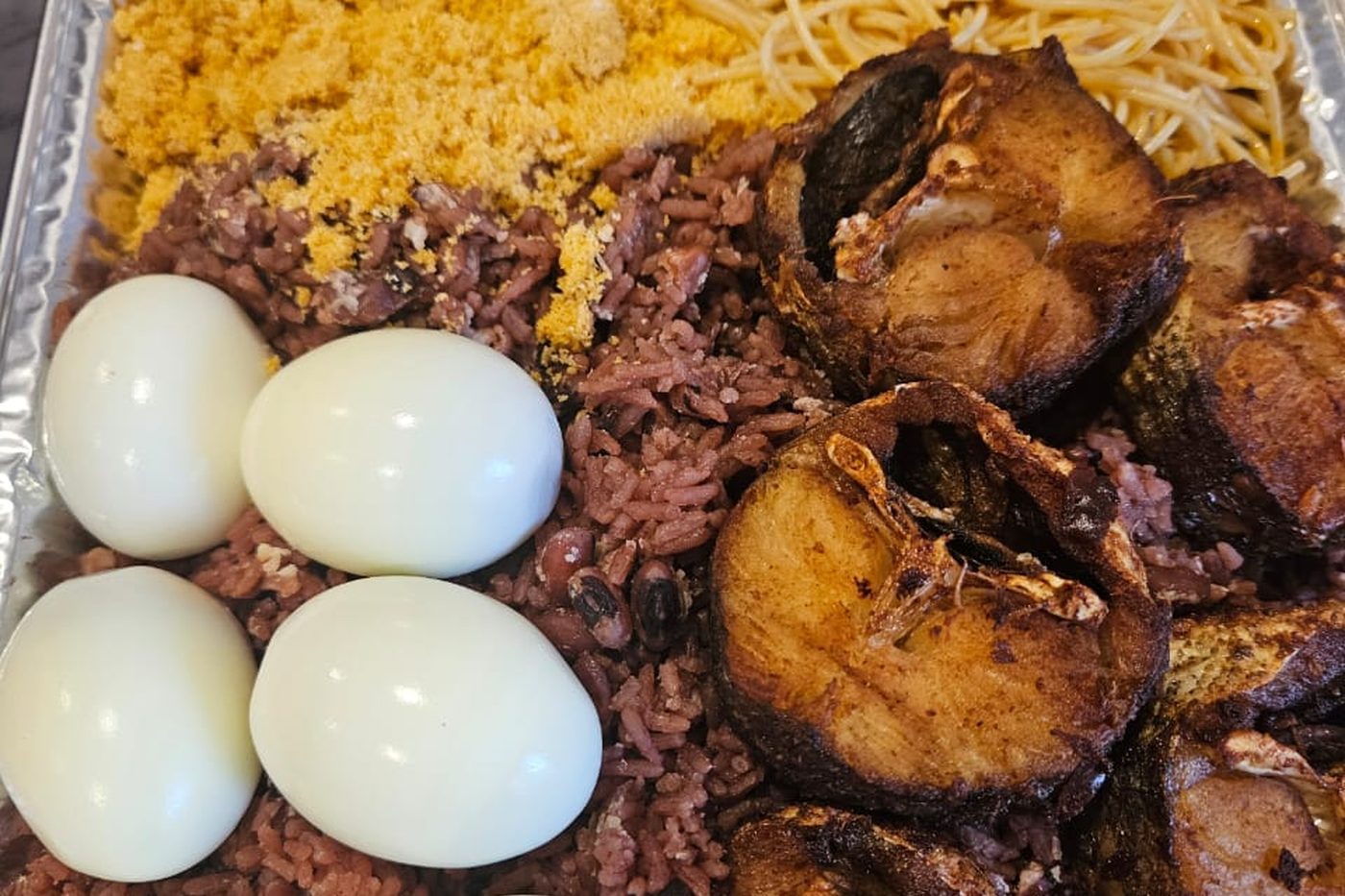 A large tray of jollof rice, noodles, plantain and boiled eggs