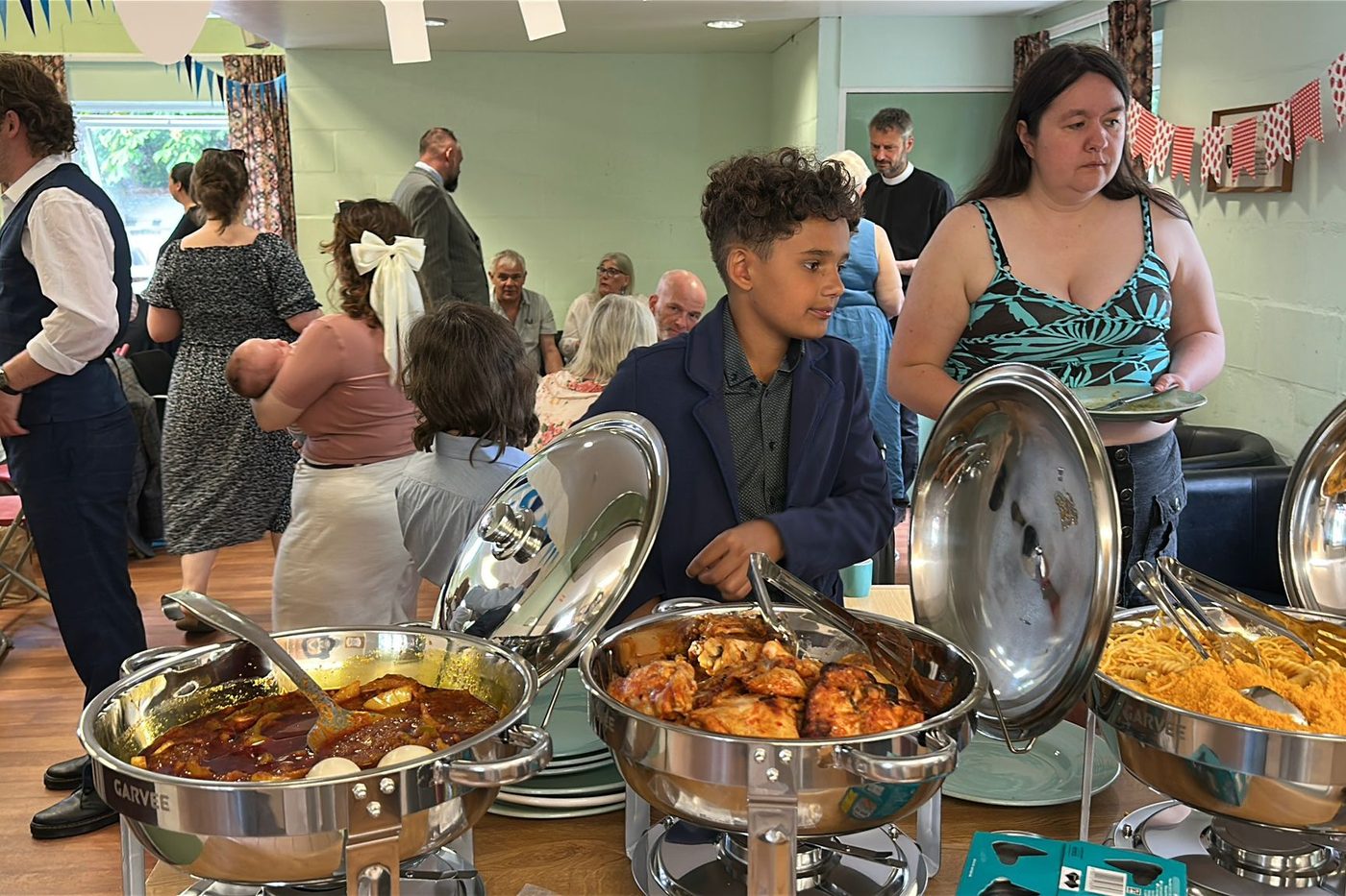 Guests serving themselves from chafing dishes of stew, grilled chicken and jollof rice