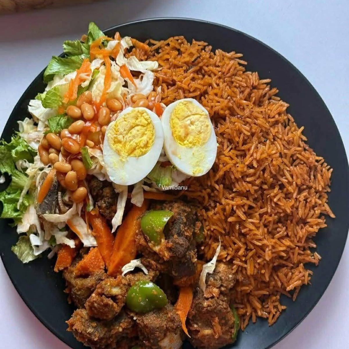 A plate of jollof rice with salad, boiled egg and chicken